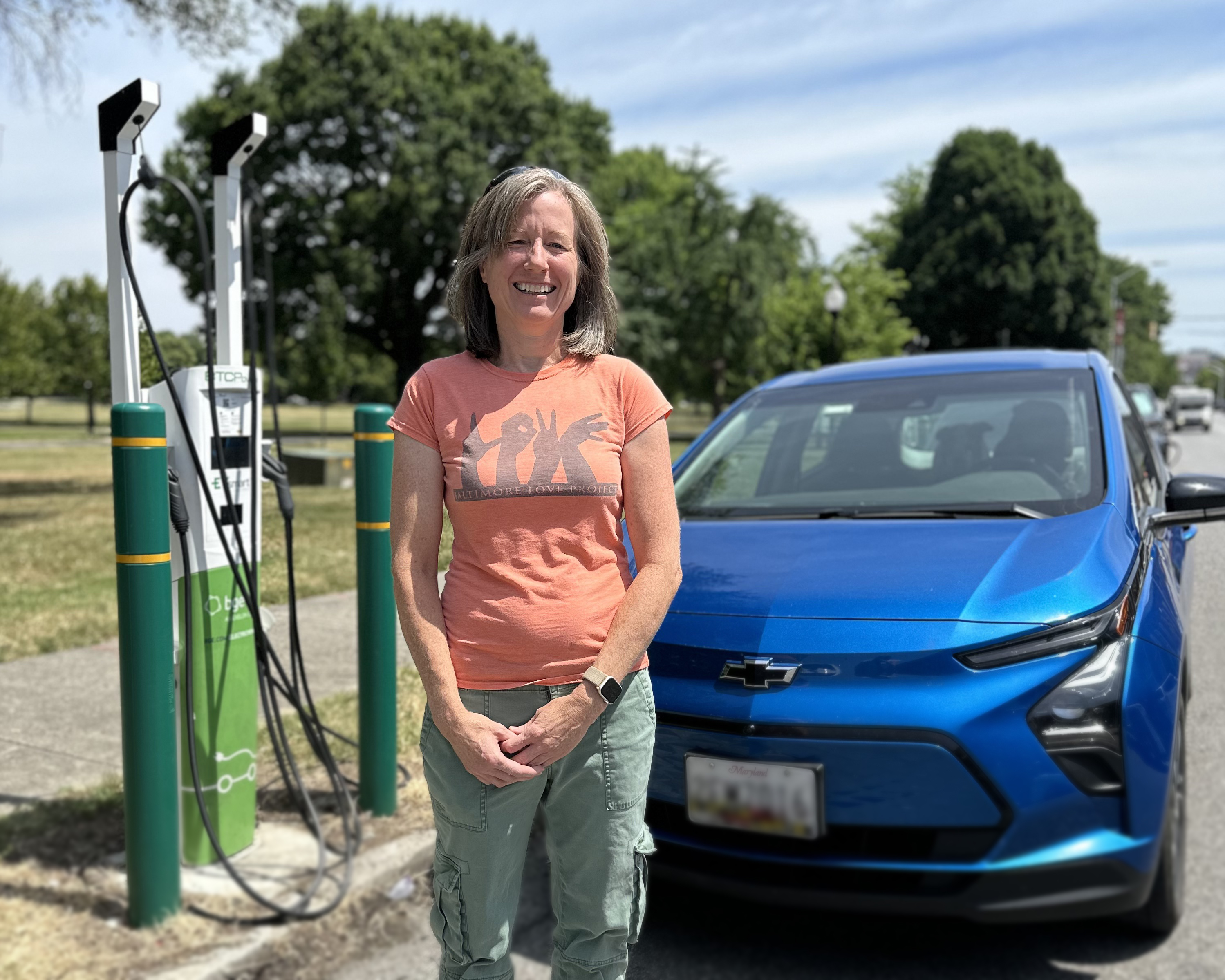 Woman standing next to electric vehicle charging station and vehicle